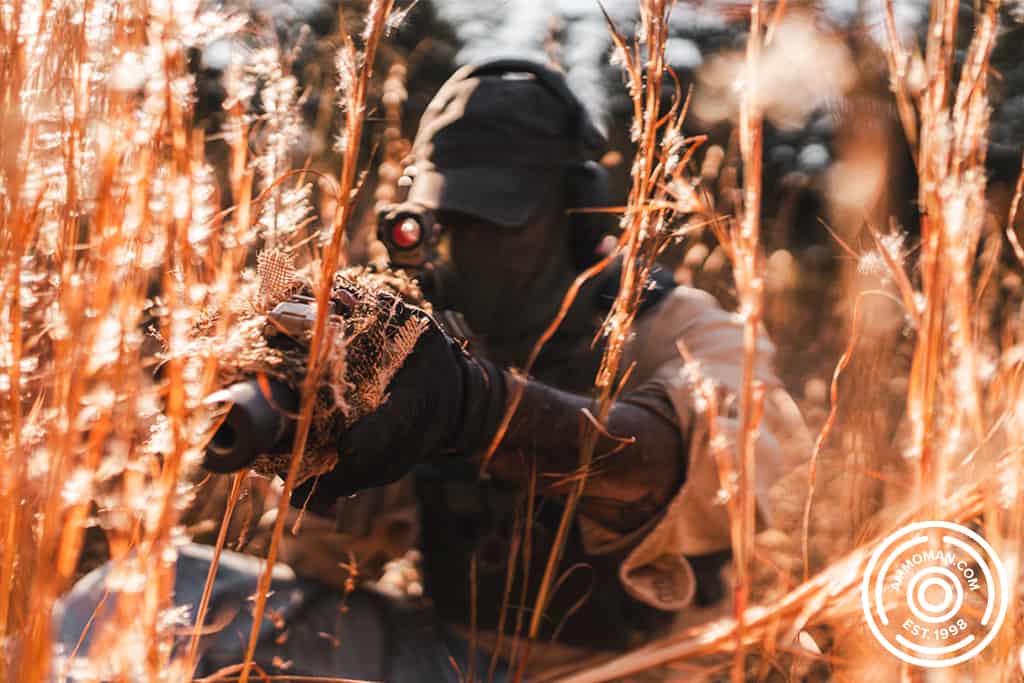 man sitting in a field with a camouflaged rifle